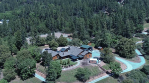 A vibrant dog park bathed in sunlight features abundant greenery with mature trees, offering ample shade for leisurely outdoor activities. In the distance is a well-equipped playground that presents an additional activity area. An inviting picnic table spreads out nearby, ideal for enjoying meals al fresco or taking relaxing breaks from play. A neatly-placed trash bin aids in maintaining the park's cleanliness for everyone's enjoyment. Dominating the scene is a generously wide dirt path gracefully curving through the expanse of grass, promising exploratory walks and lively fetch games.